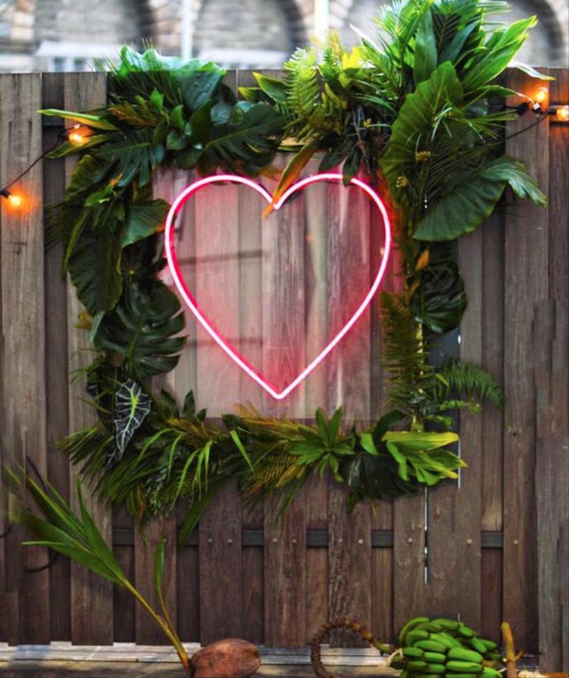 modern wedding decor idea with pink neon heart sign surrounded by greenery
